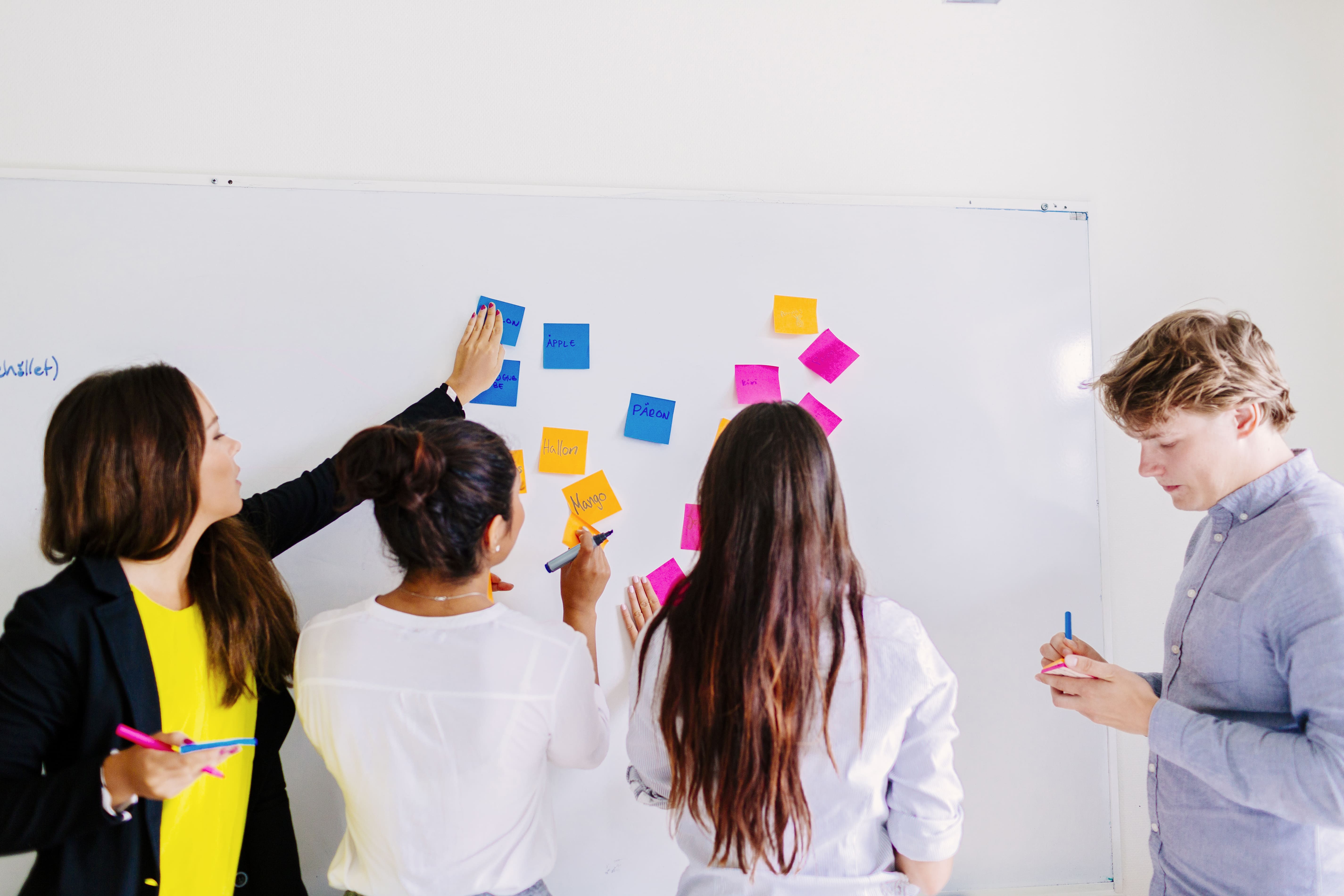 Vier Personen arbeiten gemeinsam an einem Whiteboard und sammeln Ideen.