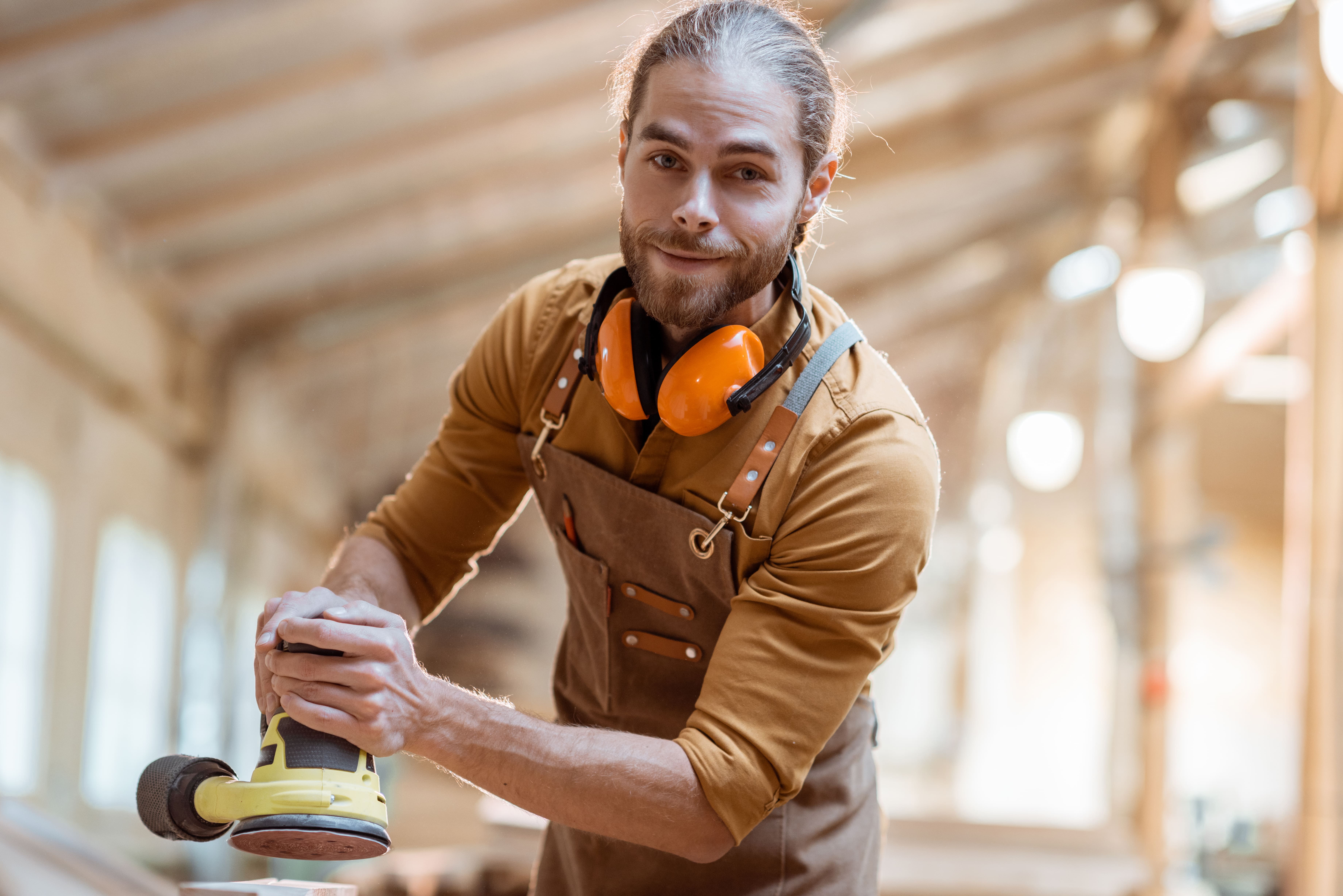 Porträtfoto eines Schreiners, der motiviert seine Tätigkeit ausübt und dabei Werkzeuge in der Werkstatt verwendet.